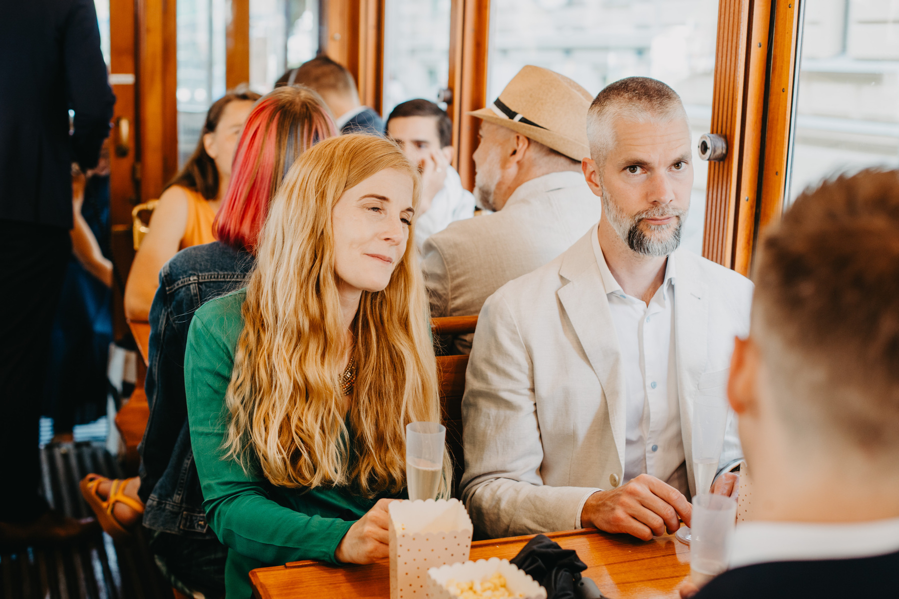 Auto-generated description: A group of people are sitting and conversing at a table, with a woman smiling and a man looking attentively at someone out of the frame.