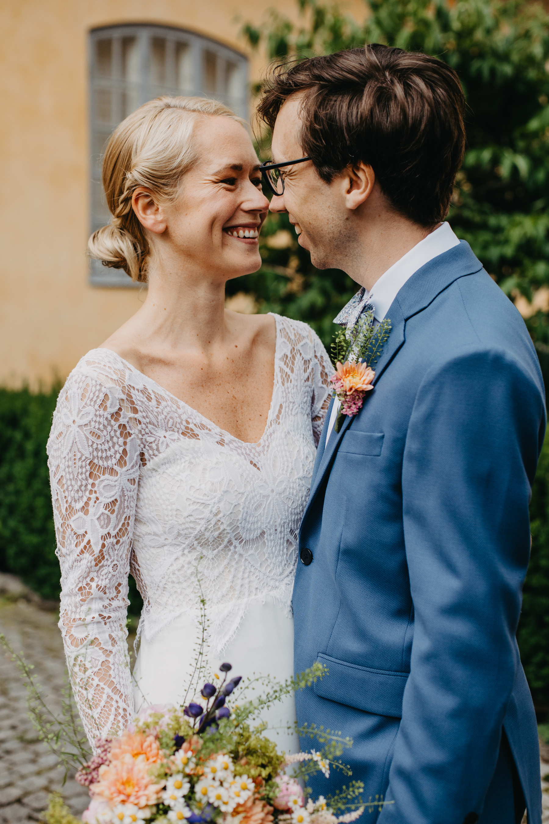 Auto-generated description: A smiling couple wearing formal attire stands close together, with the woman holding a bouquet and both appearing to be in a celebratory moment.