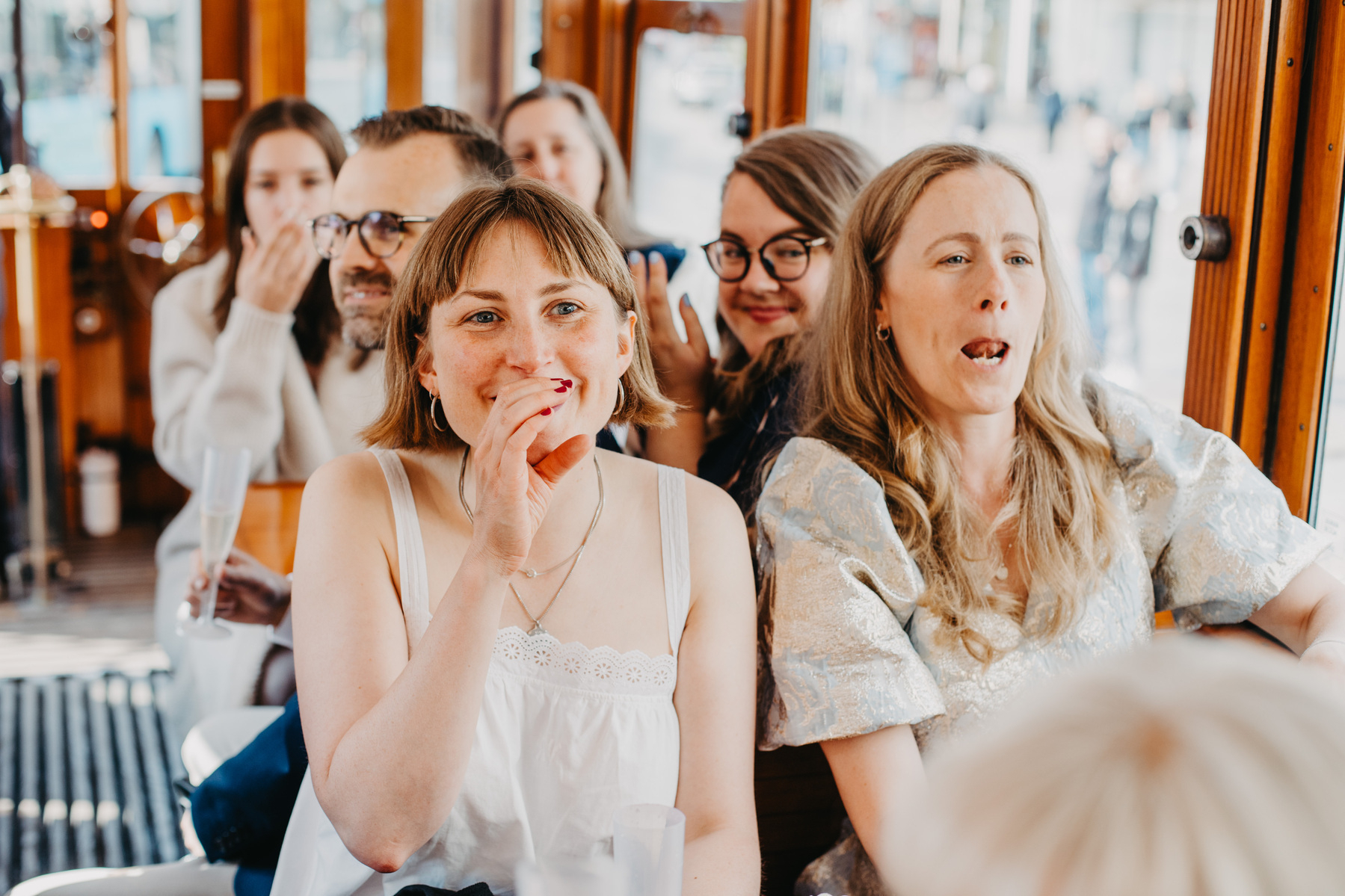 Auto-generated description: A group of people, smiling and enjoying themselves, are gathered together on what appears to be public transportation or a streetcar.