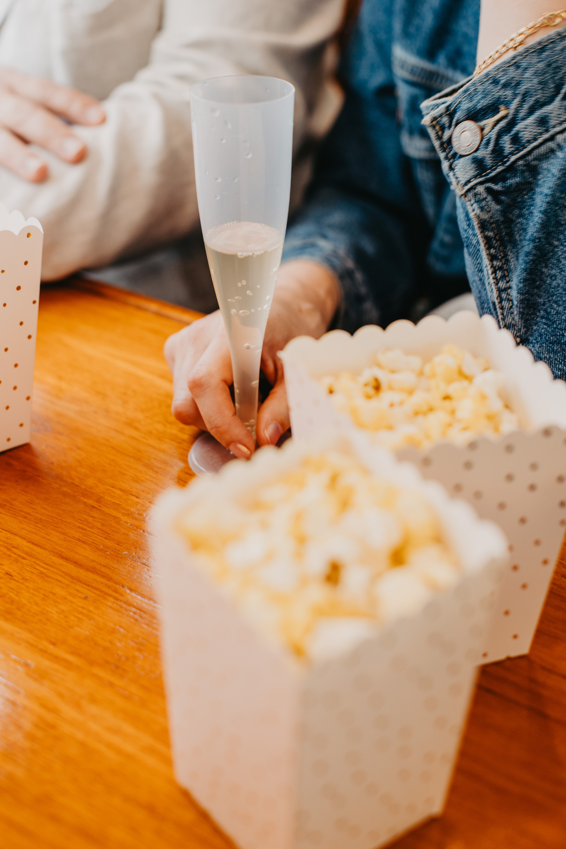 Auto-generated description: Two people are seated at a table with popcorn and one person holding a champagne flute.