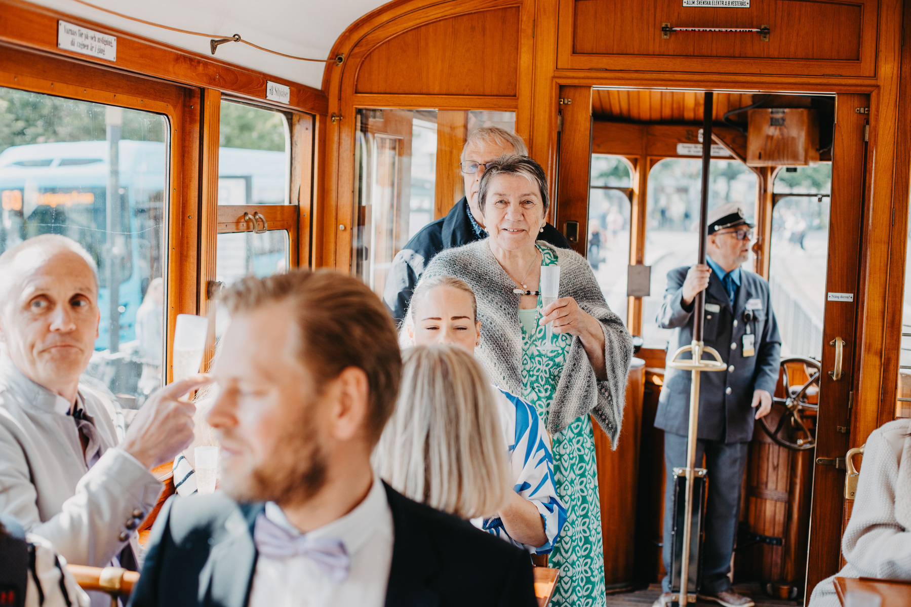 Auto-generated description: People are inside a vintage tram, with some looking out towards the camera and others engaging in conversation.