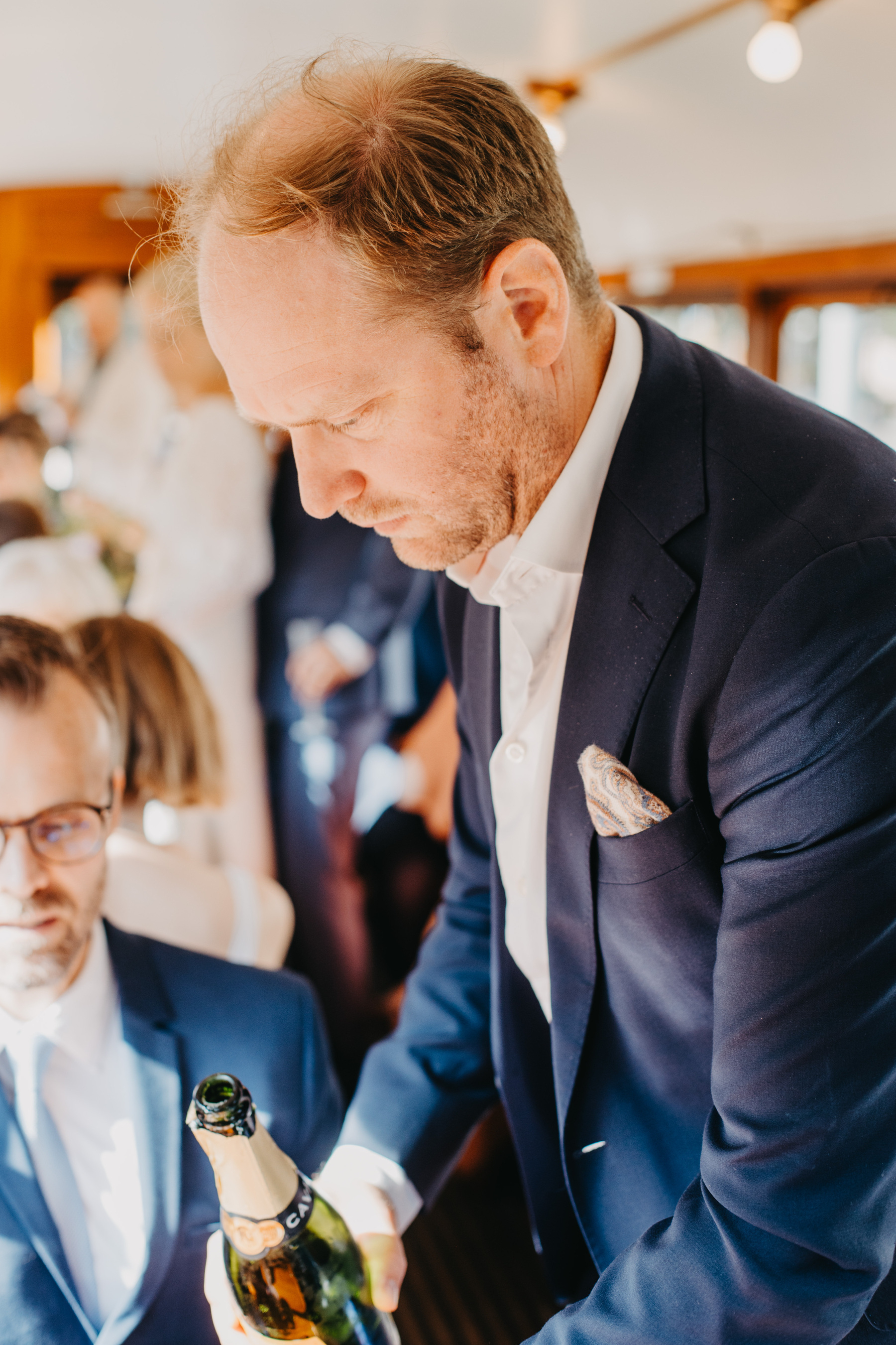 Auto-generated description: A man in a suit is pouring champagne at what appears to be a social gathering or celebration on a train carriage.