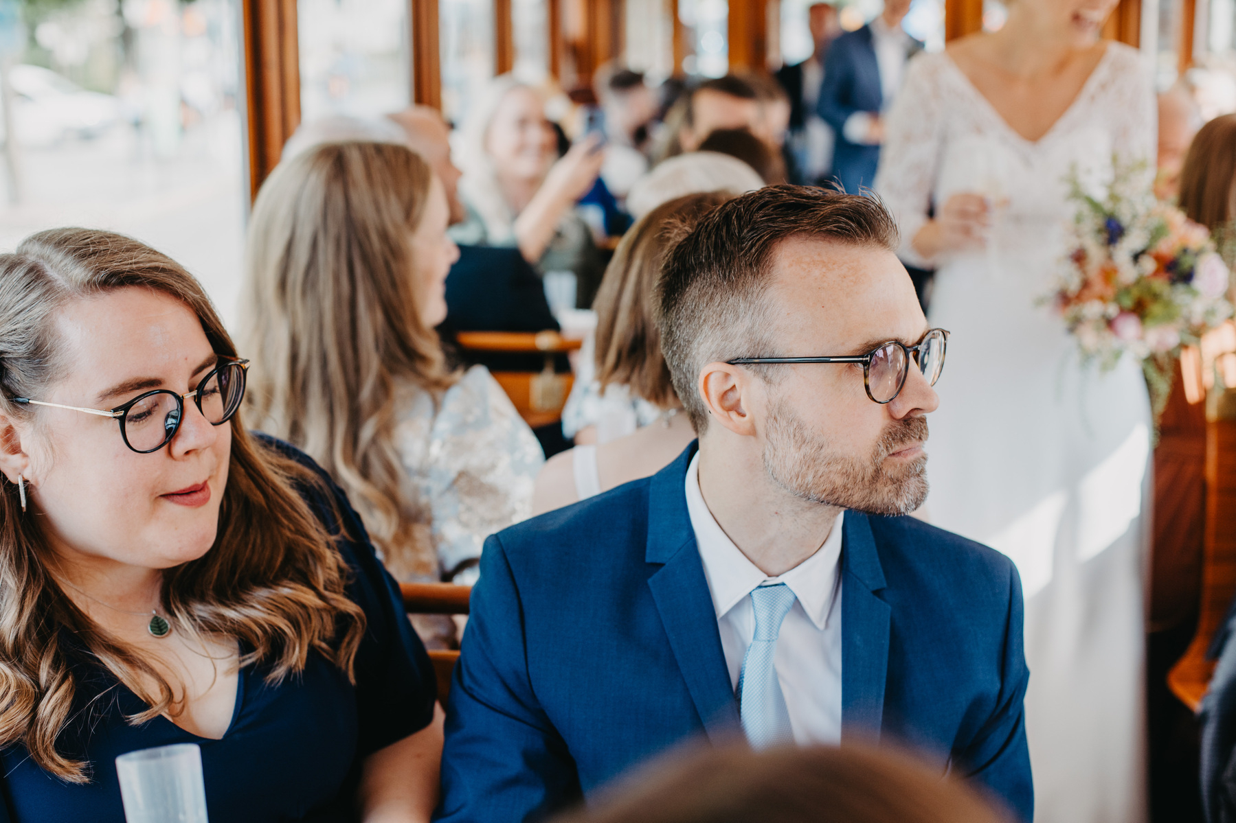 Auto-generated description: A group of formally dressed people, possibly at a wedding reception, are sitting and conversing in what appears to be a decorated venue.