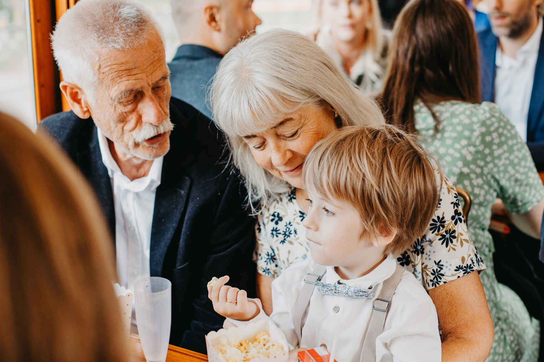 Auto-generated description: An elderly couple and a young boy are seated closely together, appearing to enjoy a moment while the boy holds a snack.