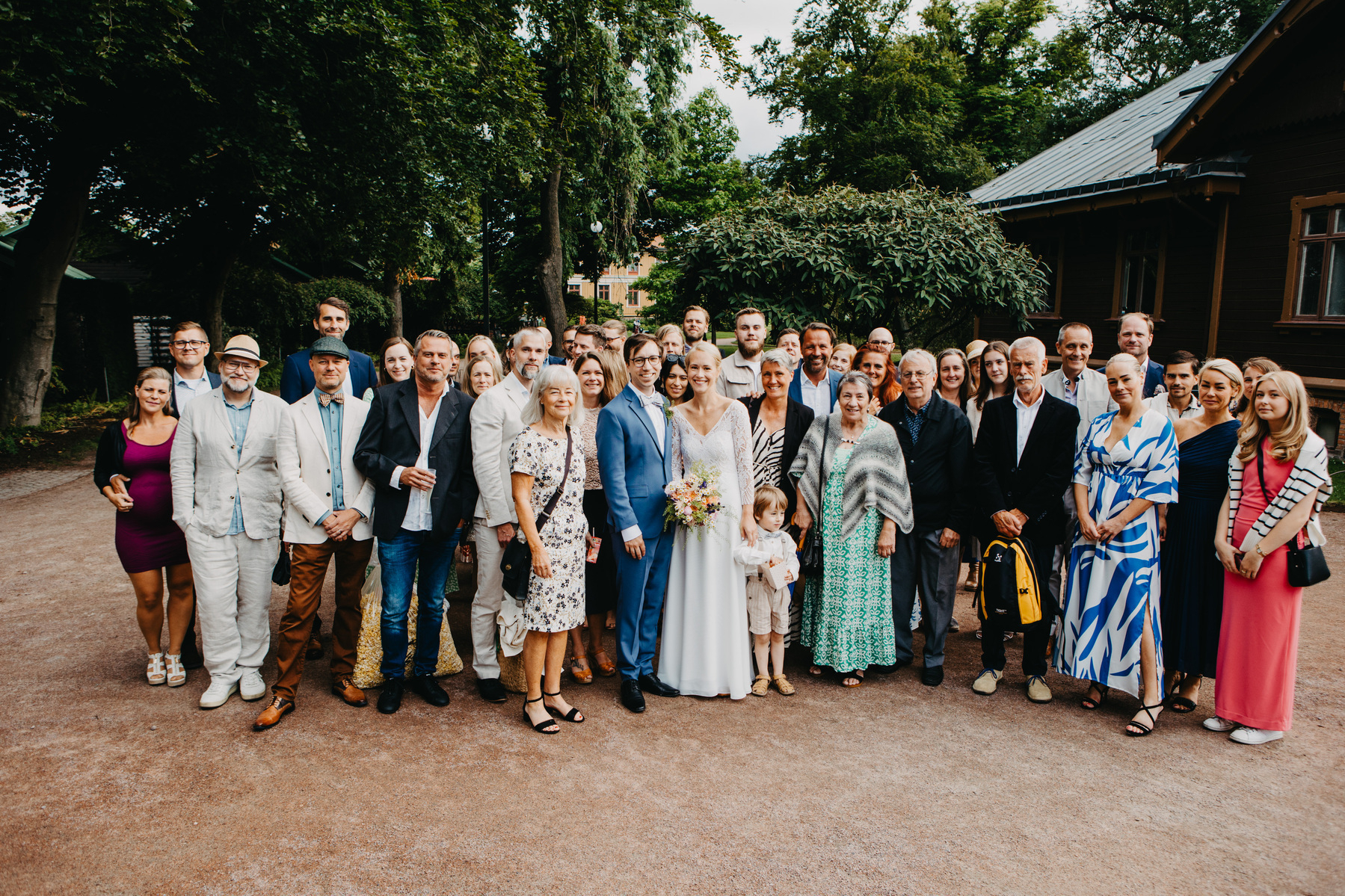 Auto-generated description: A large group of people dressed formally and gathered outdoors, posing for a wedding photo.