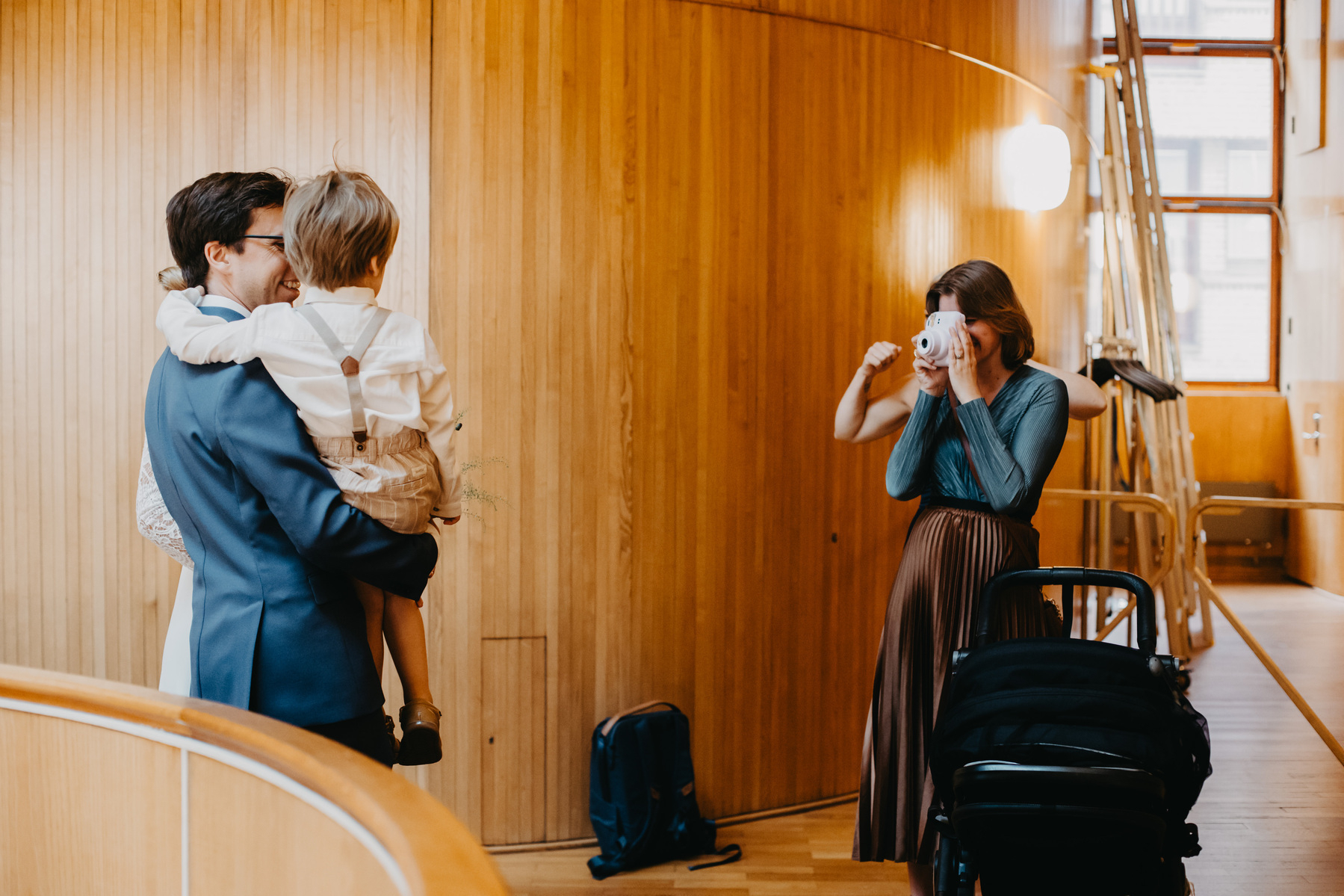 Auto-generated description: A person is taking a photo of a family in a warmly lit wooden room with a curved wall and a ladder in the background.