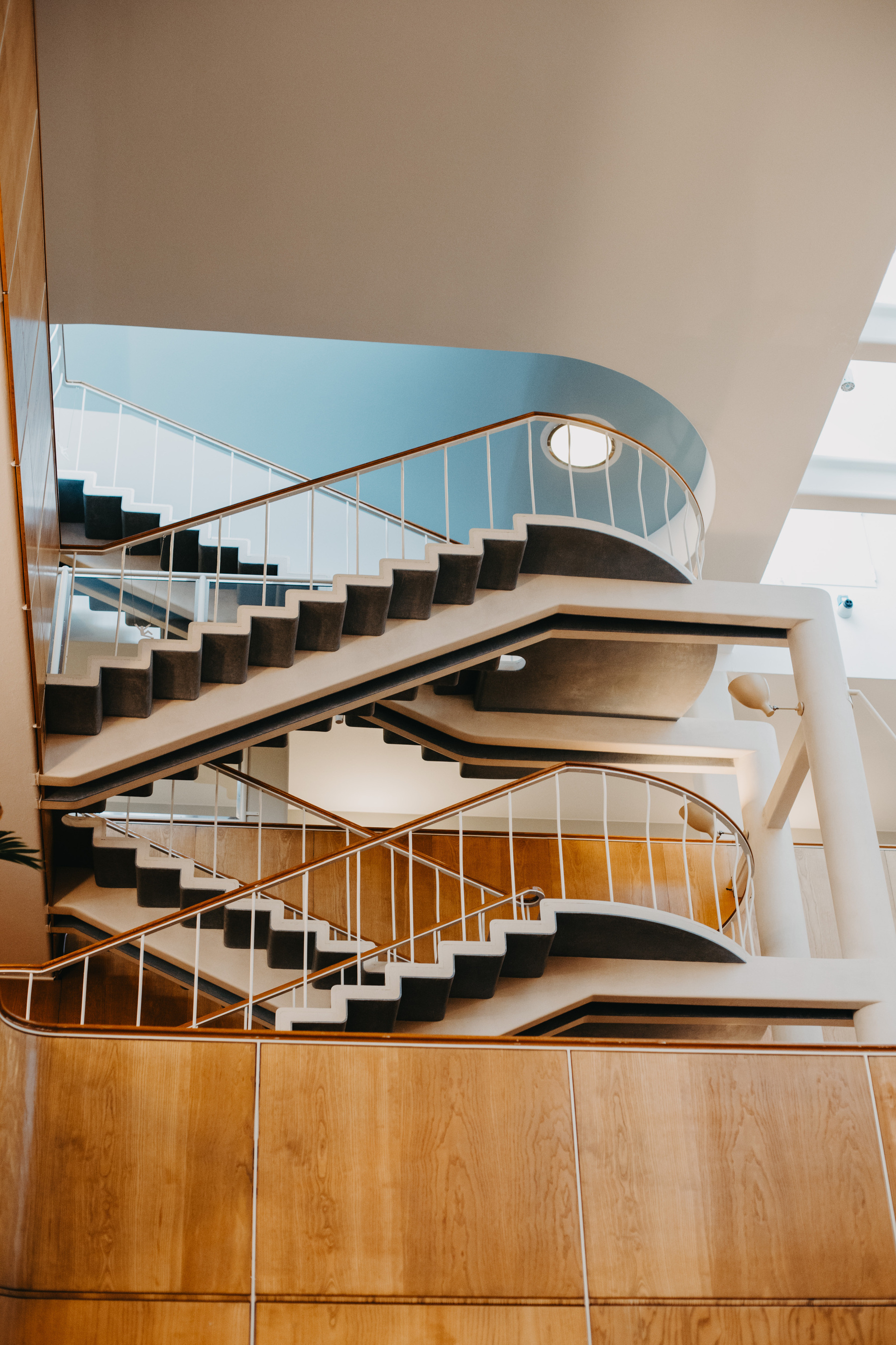 Auto-generated description: A modern multi-level staircase with sleek, curved lines and wooden panels is seen inside a building.